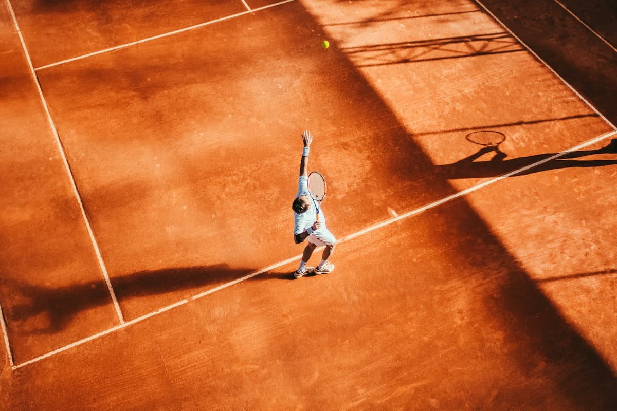 Tennis court seen from above with a player mid-serve